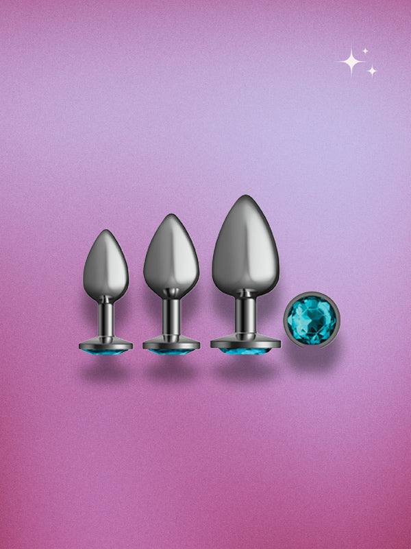 Three metallic butt plugs with a blue gemstone on a pink gradient background